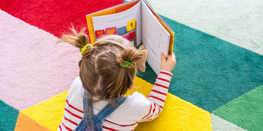 Petite fille lisant un livre sur tapis coloré