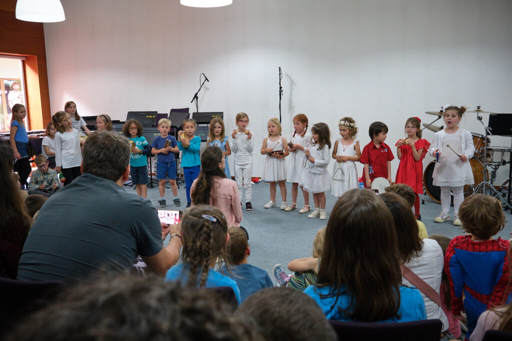 Enfants chantant avec instruments devant leurs parents