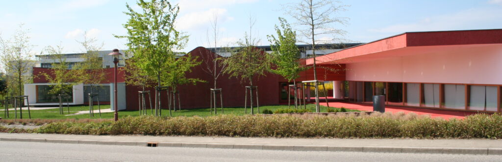 Bâtiment moderne rouge entouré d’arbres et pelouse