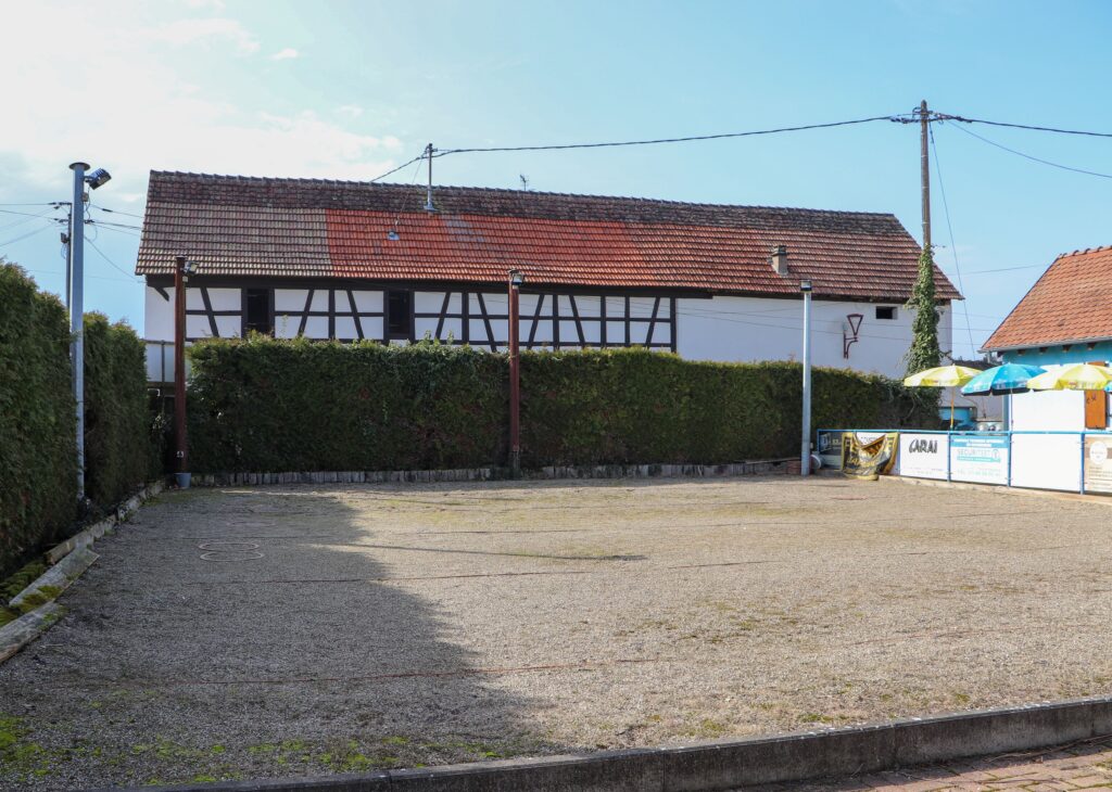 Terrain de pétanque en gravier devant une maison à colombages à Behlenheim